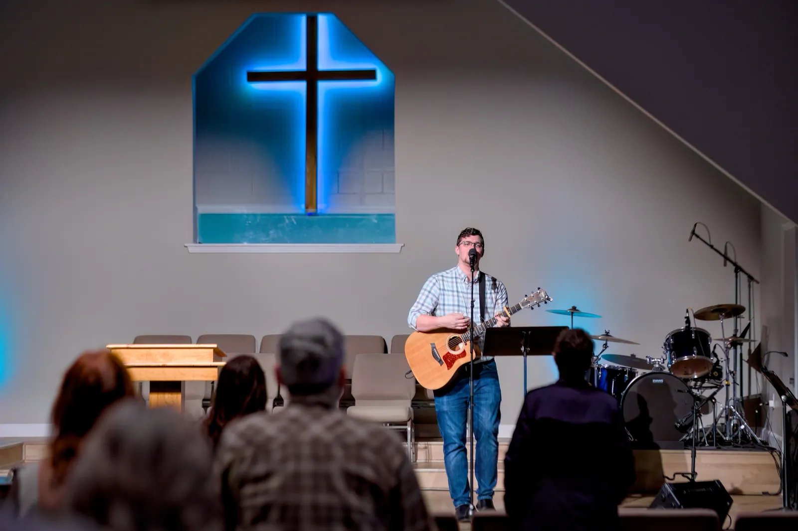 Jonathan Glisson leading worship with an acoustic guitar in front of an illuminated cross